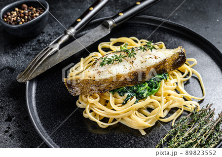 Baked Halibut fish steak and Spaghetti pasta with spinach. Black background. Top view Baked Halibut fish steak and Spaghetti pasta with spinach. Black background. Top view 89823552