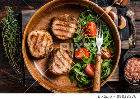 Roasted pork medallions steaks from tenderloin fillet with vegetable salad in wooden plate. Wooden background. Top view 89823576
