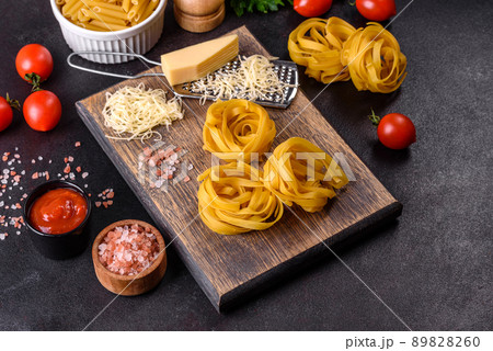 Raw tagliatelle paste with grated cheese, cherry tomatoes, spices and herbs on a wooden cutting board Raw tagliatelle paste with grated cheese, cherry tomatoes, spices and herbs on a wooden cutting board 89828260
