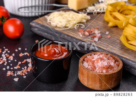 Raw tagliatelle paste with grated cheese, cherry tomatoes, spices and herbs on a wooden cutting board 89828263