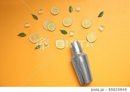 Flat lay composition with fresh juicy limes, ice cubes and cocktail shaker on yellow background 89829849