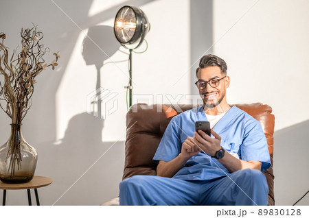 Joyous physician in eyeglasses resting in the armchair 89830128