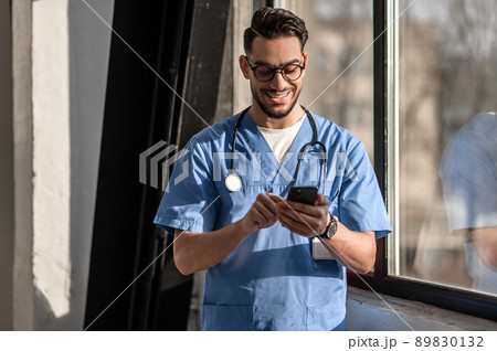 Pleased physician texting someone on his cellphone 89830132