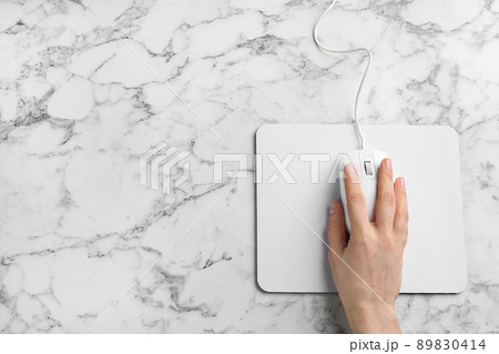 Woman using modern wired optical mouse on white marble table, top view. Space for text 89830414