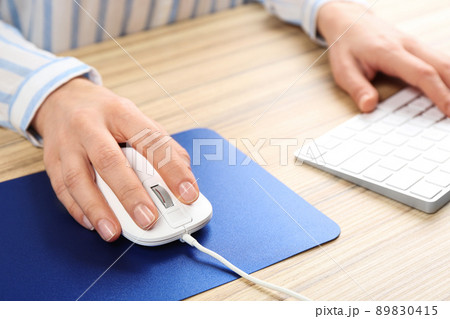 Woman using modern wired optical mouse at office table, closeup 89830415