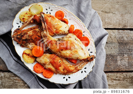 Roasted Rabbit Haunches in Pan with Stewed Vegetables on Rustic Wooden Table Surface 89831676
