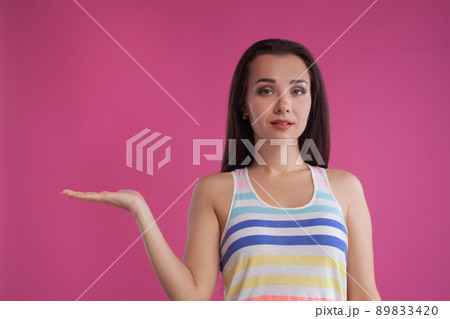 Brunette woman with long hair, dressed in colorful striped shirt, posing against pink studio background. Sincere emotions. Close-up. Brunette woman with long hair, dressed in colorful striped shirt, posing against pink studio background. Sincere emotions. Close-up. 89833420