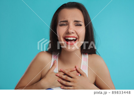 Brunette woman with long hair, dressed in colorful striped shirt, posing against blue studio background. Sincere emotions. Close-up. Brunette woman with long hair, dressed in colorful striped shirt, posing against blue studio background. Sincere emotions. Close-up. 89833448