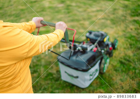 Mowing the grass with a lawn mower in early spring or summer. Gardener woman cuts the lawn in the garden. Worker mowing tall grass with electric or petrol lawn trimmer in city park or backyard. 89833683
