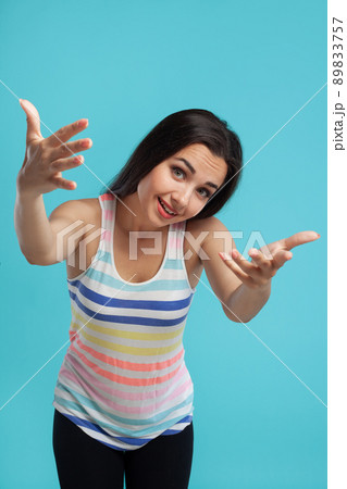 Brunette woman with long hair, dressed in striped shirt and black leggings, posing against blue studio background. Sincere emotions. Close-up. 89833757