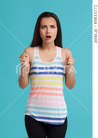 Brunette woman with long hair, dressed in striped shirt and black leggings, posing against blue studio background. Sincere emotions. Close-up. 89833772