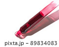 Liquid red oil serum drop in pipette isolated on white background. Retinol, aha acid, collagen skincare fluid, close up photo with shallow depth of field. Transparent crimson essence in dropper 89834083