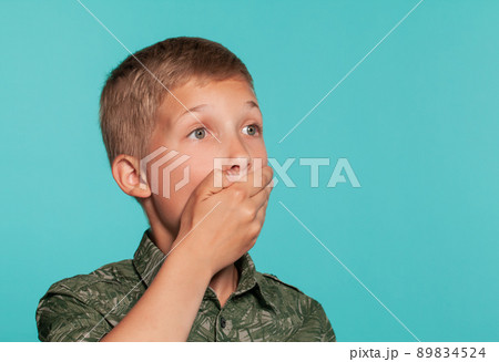 Close-up portrait of a blonde teenage boy in a green shirt with palm print posing against a blue studio background. Concept of sincere emotions. Close-up portrait of a blonde teenage boy in a green shirt with palm print posing against a blue studio background. Concept of sincere emotions. 89834524