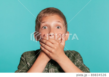 Close-up portrait of a blonde teenage boy in a green shirt with palm print posing against a blue studio background. Concept of sincere emotions. Close-up portrait of a blonde teenage boy in a green shirt with palm print posing against a blue studio background. Concept of sincere emotions. 89834526