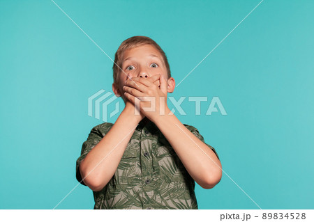 Close-up portrait of a blonde teenage boy in a green shirt with palm print posing against a blue studio background. Concept of sincere emotions. 89834528