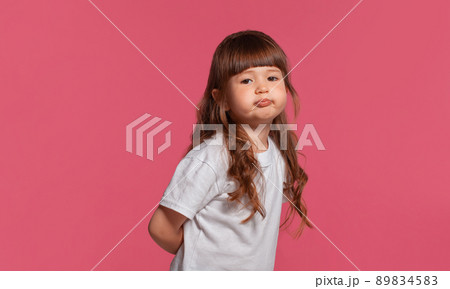 Close-up portrait of a little brunette girl dressed in a white t-shirt posing against a pink studio background. Sincere emotions concept. 89834583