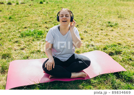 Beautiful young redhead woman relaxing on Yoga Mat after Training. Happy girl with Earphones Listening Music. Sport or yoga concept 89834669