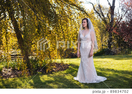 White Caucasian Adult Woman in a Wedding Dress standing outside in nature. White Caucasian Adult Woman in a Wedding Dress standing outside in nature. 89834702