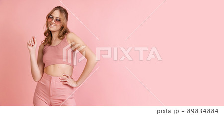 Monochrome portrait of young attractive woman in shorts and crop top isolated on pink background. Concept of beauty, art, fashion, youth. Flyer 89834884