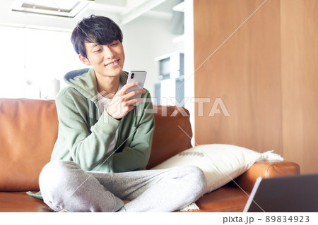 ソファの上であぐらをかいてスマホを見る若い男性 89834923