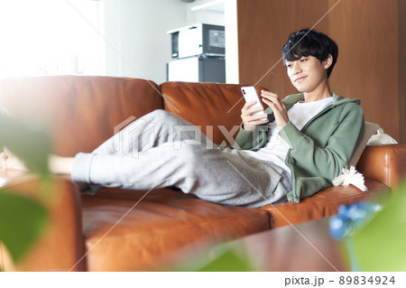 自宅のソファで横になってスマホを触る若い男性 89834924