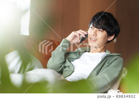 自宅のソファで横になってスマホ通話する若い男性 89834932