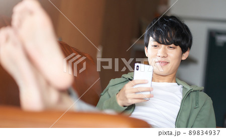 ソファにもたれてスマホを見る若い男性 89834937