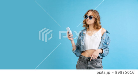 Young beautiful girl in casual style outfit using phone isolated on blue background. Concept of beauty, art, fashion, youth, fall collection 89835016