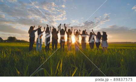 Silhouette of friends of 11 girls waving their hands at sunset in the field. Silhouette of friends of 11 girls waving their hands at sunset in the field. 89837575