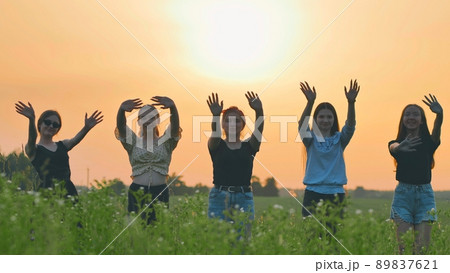 Girls friends waving their hands to the setting sun on the background of the sunset. Girls friends waving their hands to the setting sun on the background of the sunset. 89837621