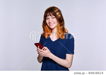 Beautiful smiling teenage female with smartphone in her hands looking at camera Beautiful smiling teenage female with smartphone in her hands looking at camera 89838624
