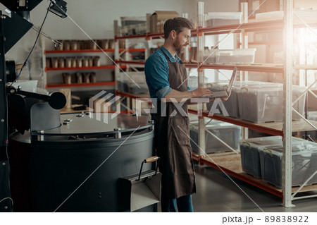Barista on small coffee factory working laptop on background of coffee roasting machine 89838922