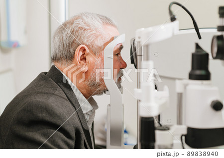 examines elderly man's eye on screen of autorefractometer.  89838940