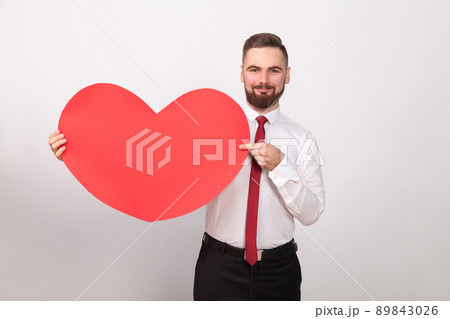 Perfect businessman smiling, pointing finger at big red heart. Indoor, studio shot, isolated on gray background 89843026