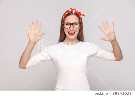 hey, nice to see you. portrait of beautiful emotional young woman in white t-shirt with freckles, black glasses, red lips and head band. indoor studio shot, isolated on light gray background. hey, nice to see you. portrait of beautiful emotional young woman in white t-shirt with freckles, black glasses, red lips and head band. indoor studio shot, isolated on light gray background. 89843028