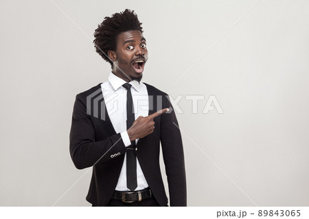 African businessman pointing finger at copy space, looking at camera with shocked face. Studio shot, gray background 89843065