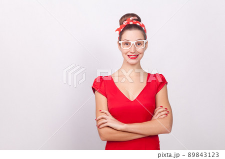 Cheerful beautiful woman in red dress and white glasses smiling. Indoor, studio shot, isolated on gray background Cheerful beautiful woman in red dress and white glasses smiling. Indoor, studio shot, isolated on gray background 89843123