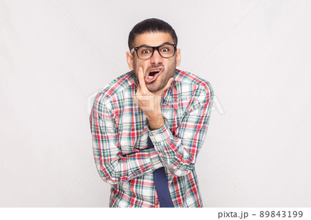 Portrait of сrazy shocked bearded businessman in colorful checkered shirt, blue tie and eyeglasses standing touching face and looking at camera. indoor studio shot, isolated on light grey background. Portrait of сrazy shocked bearded businessman in colorful checkered shirt, blue tie and eyeglasses standing touching face and looking at camera. indoor studio shot, isolated on light grey background. 89843199