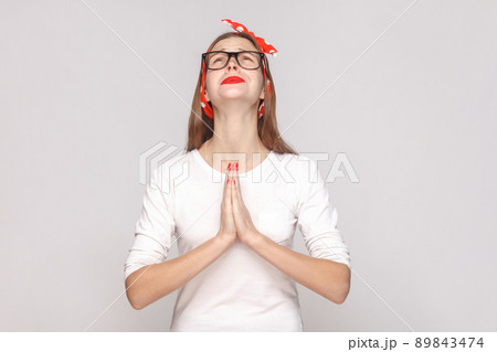 Oh my God please help me. portrait of beautiful emotional young woman in white t-shirt with freckles, black glasses, red lips and head band. indoor studio shot, isolated on light gray background. 89843474
