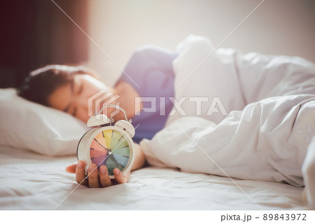 Morning alarm clock in the hand of an Asian woman sleeping soundly in bed in the bedroom. Morning alarm clock in the hand of an Asian woman sleeping soundly in bed in the bedroom. 89843972