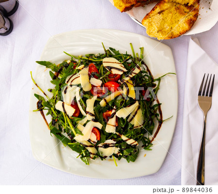 Green arugula salad with cheese, tomatoes and seasoning 89844036