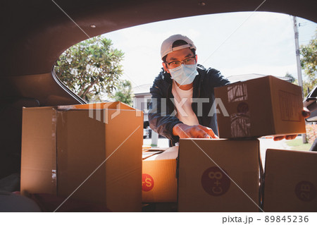 Asian postman with a hygiene protective face mask picking up a parcel package or parcel box from the truck for deliver to customer's door. New Normal concept during covid-19 or coronavirus pandemic Asian postman with a hygiene protective face mask picking up a parcel package or parcel box from the truck for deliver to customer's door. New Normal concept during covid-19 or coronavirus pandemic 89845236