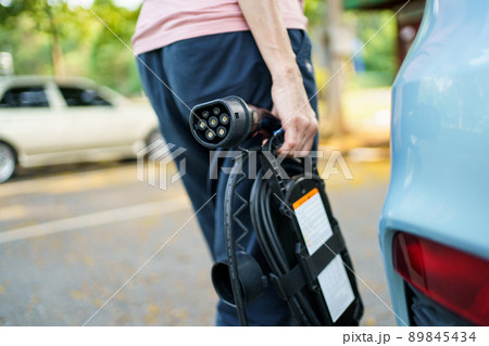 Unrecognizable woman holding the portable EV emergency charging adapter and preparing to charge the EV car. Electric Vehicle charging adapter close up with copyspace. 89845434