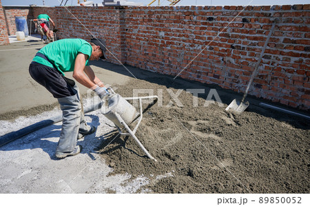 Male worker using concrete screed mixer machine while preparing sand-cement mix for floor screed. Man builder working with professional floor screed equipment at construction site. 89850052