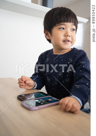 リビングのテーブルの上で2台のスマホを操作するデジタルネイティブ世代の4歳男児 89850422
