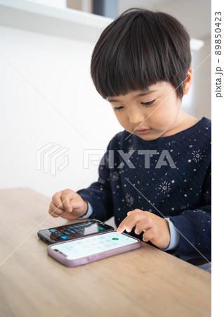リビングのテーブルの上で2台のスマホを操作するデジタルネイティブ世代の4歳男児 89850423