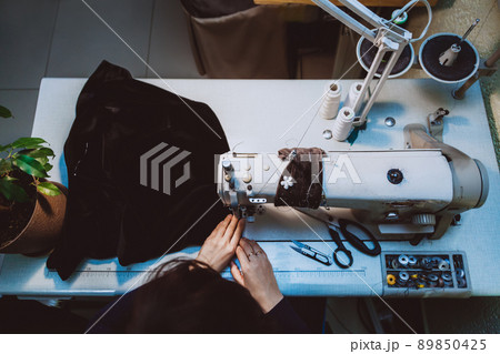 A woman tailor sews clothes - a fashionable jacket made of velvet fabric on a sewing machine in her atelier 89850425