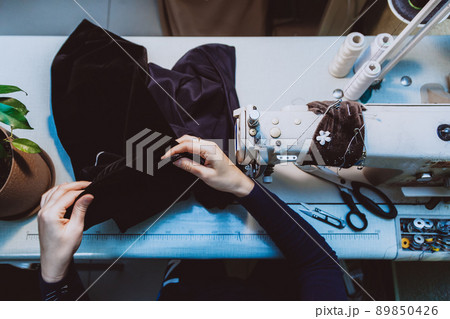 A woman tailor sews clothes - a fashionable jacket made of velvet fabric on a sewing machine in her atelier 89850426
