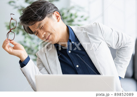 デスクワーク中に背中に手を当てる体調不良の男性 デスクワーク中に背中に手を当てる体調不良の男性 89852089