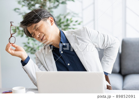 デスクワーク中に背中に手を当てる体調不良の男性 89852091